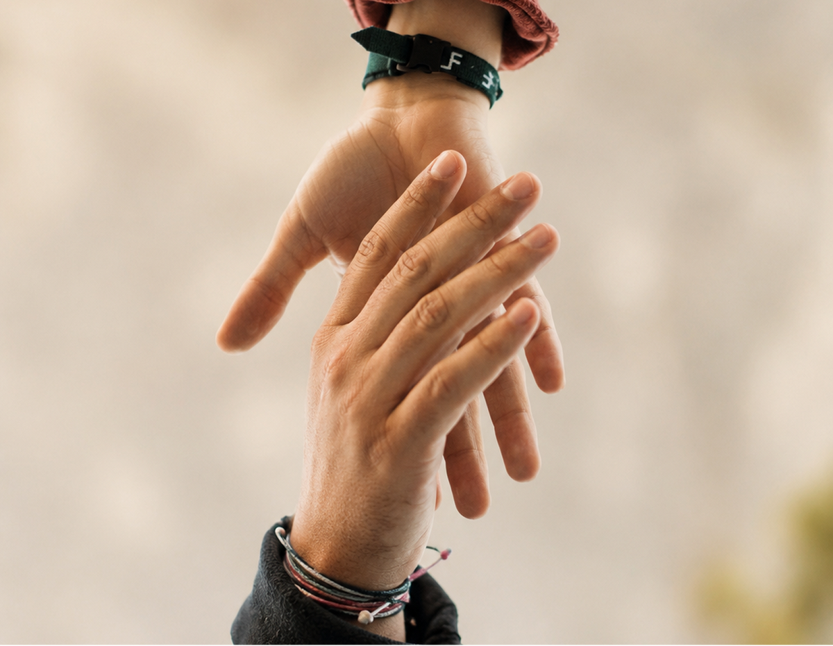 Two hands gently touching, each wearing a thin black bracelet. The background is a soft, out-of-focus beige tone.